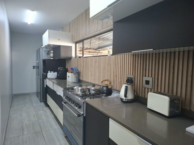 Modern galley-style kitchen featuring gas stove, stone countertops, and contemporary slatted timber wall paneling with ample built-in cabinetry.