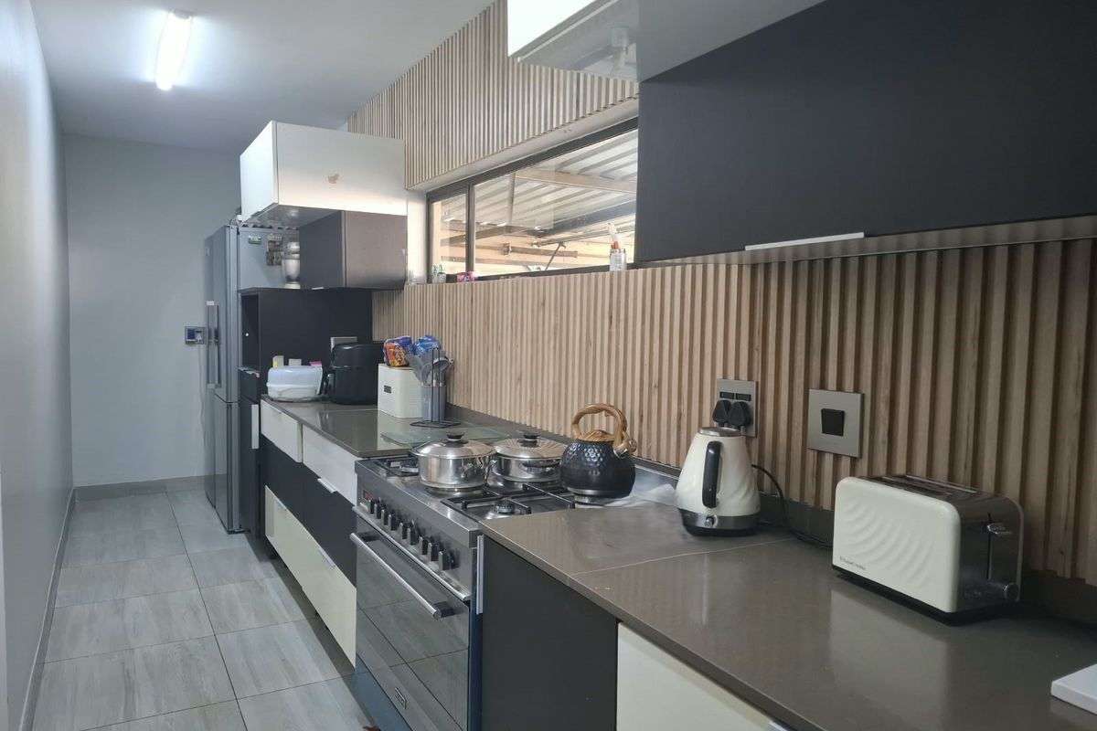 Modern galley-style kitchen featuring gas stove, stone countertops, and contemporary slatted timber wall paneling with ample built-in cabinetry.
