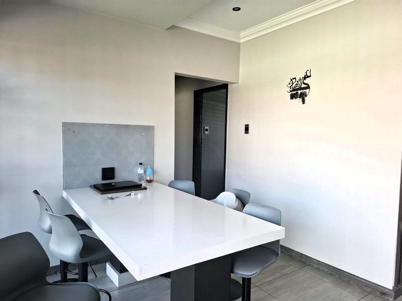 A modern dining area featuring a sleek built-in stone table, tiled flooring, and recessed ceiling lighting with elegant cove molding.