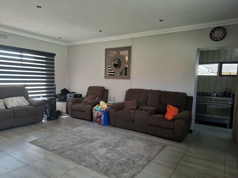 Spacious living room featuring tiled flooring, recessed downlights, and zebra blinds, with an open transition to the adjacent kitchen area.