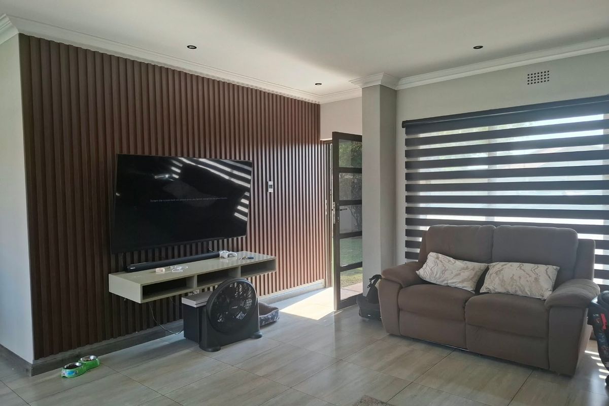 A modern living room featuring stylish slatted wood wall paneling, neutral tiled flooring, and contemporary zebra blinds for adjustable natural light.