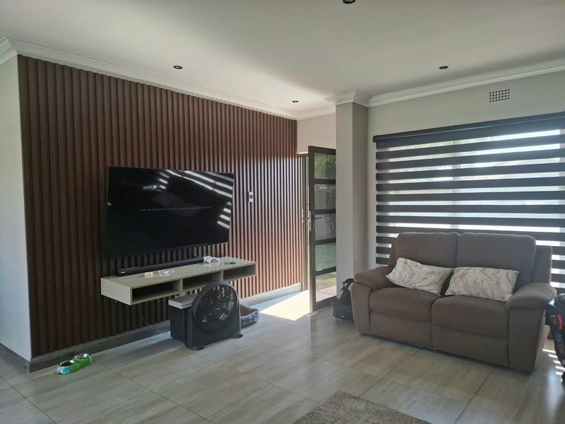 A modern living room featuring stylish slatted wood wall paneling, neutral tiled flooring, and contemporary zebra blinds for adjustable natural light.