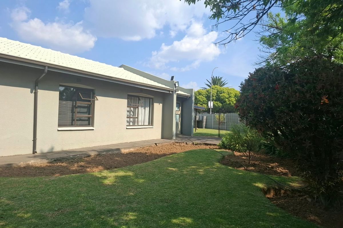 A view of the rear exterior of the house featuring a well-maintained lawn, paved walkway, and established garden beds.