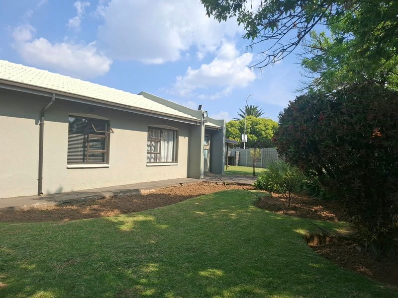 A view of the rear exterior of the house featuring a well-maintained lawn, paved walkway, and established garden beds.
