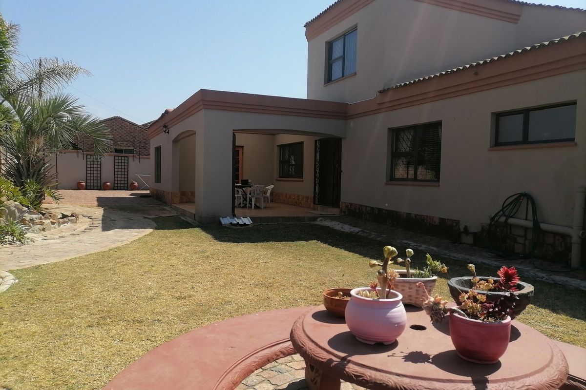 Rear view of the house featuring a covered patio area, paved garden pathways, and established exterior wall finishes.