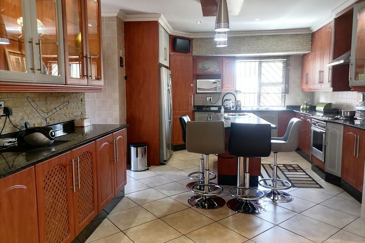 Spacious kitchen featuring warm wood cabinetry, granite countertops, a central island with breakfast bar seating, and tiled flooring throughout.