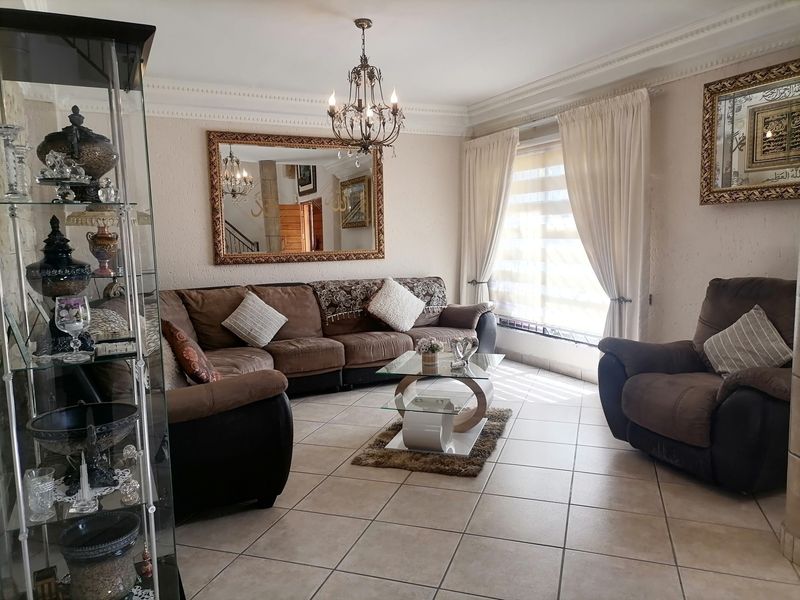 A well-maintained living room featuring tiled flooring, decorative ceiling cornices, and a classic chandelier, providing a comfortable and inviting space.