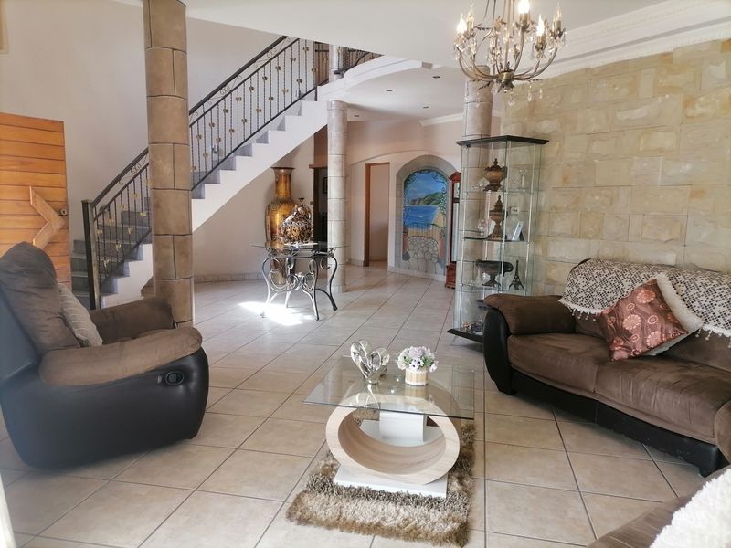 Spacious living area featuring a stone accent wall, tiled flooring, and an elegant staircase with wrought iron detailing.