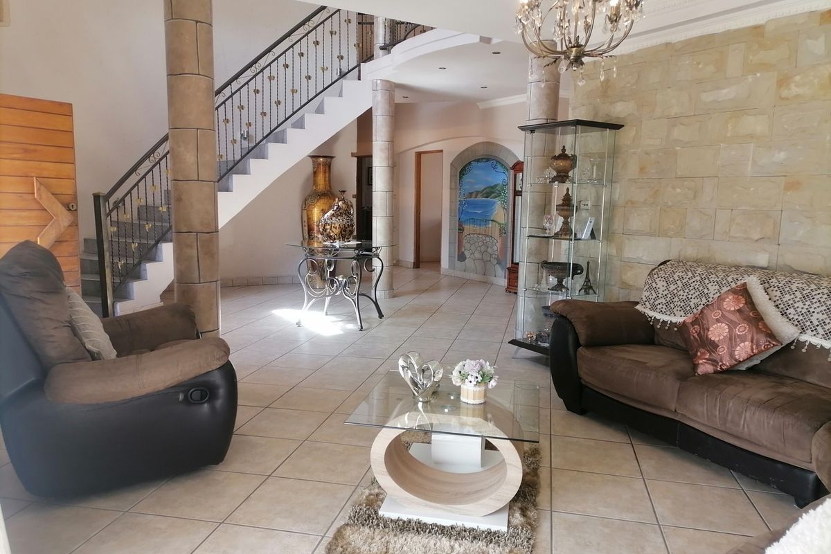 Spacious living area featuring a stone accent wall, tiled flooring, and an elegant staircase with wrought iron detailing.