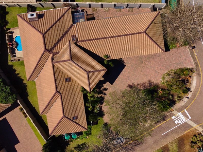 Aerial view of the property showcasing the tiled roof structure, paved driveway, swimming pool, and surrounding garden area.