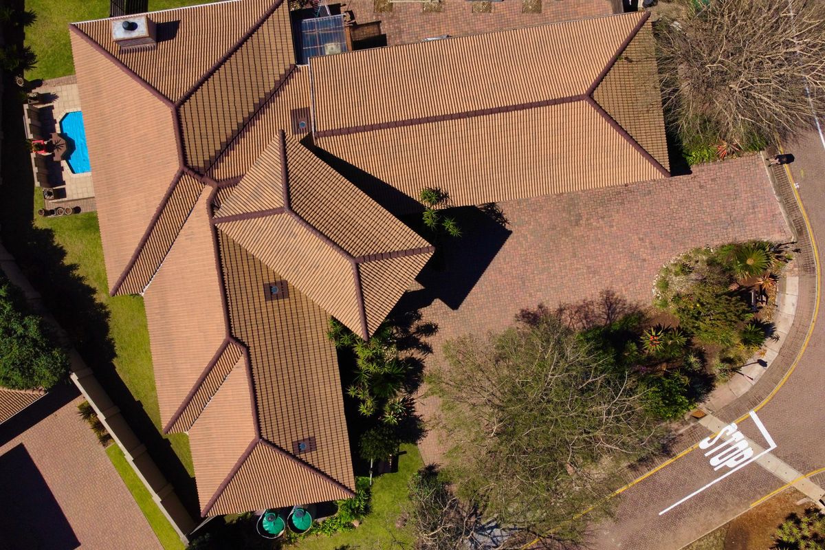 Aerial view of the property showcasing the tiled roof structure, paved driveway, swimming pool, and surrounding garden area.