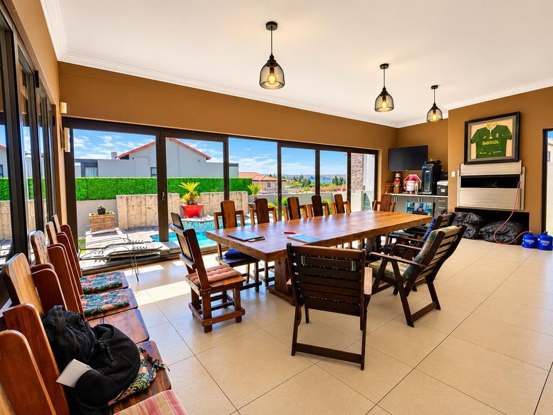 Spacious open-plan living and dining area featuring large sliding glass doors that open to the pool area, complemented by modern pendant lighting and tiled floors.