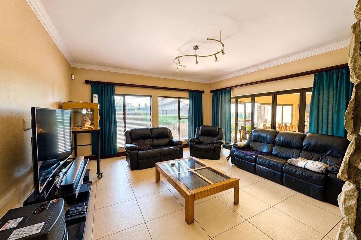 Spacious living room featuring large format floor tiles, crown molding, and expansive sliding glass doors providing natural light and access to the patio.