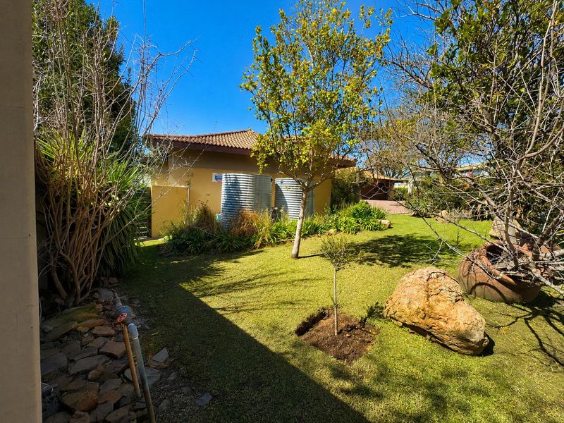 A well-maintained rear garden featuring established trees, lawn, and two corrugated metal water tanks against the house exterior.