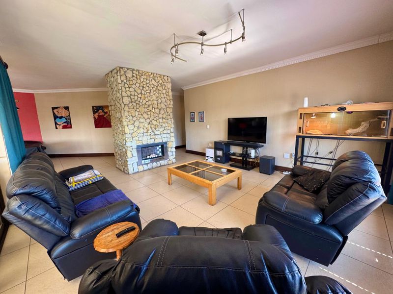 Spacious living room featuring a central stone-clad fireplace, neutral tiled flooring, and decorative cove cornicing.