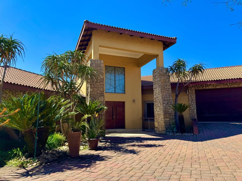 Front elevation of a house featuring stone cladding, a tiled roof, a paved driveway, and a prominent double-door entrance.