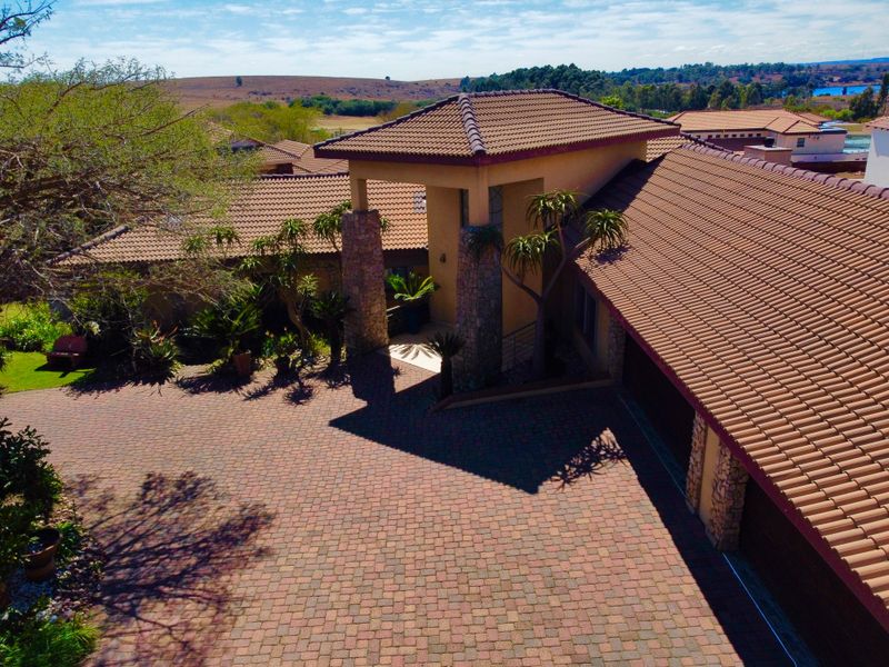 Aerial view of the property featuring a tiled roof, stone-clad entrance pillars, and a spacious paved driveway leading to the garage.