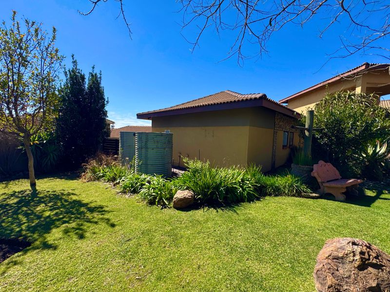 A well-maintained rear garden area featuring a lawn, established landscaping, and two exterior water tanks against the side of the house.