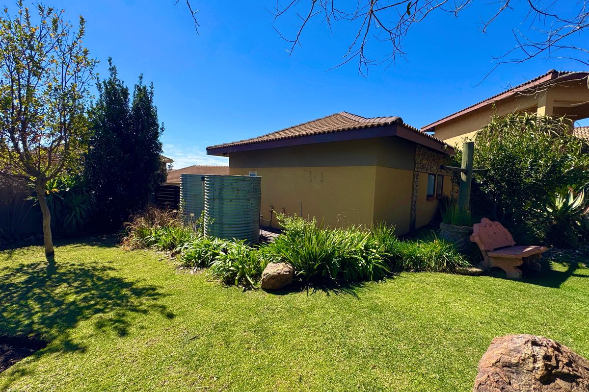 A well-maintained rear garden area featuring a lawn, established landscaping, and two exterior water tanks against the side of the house.