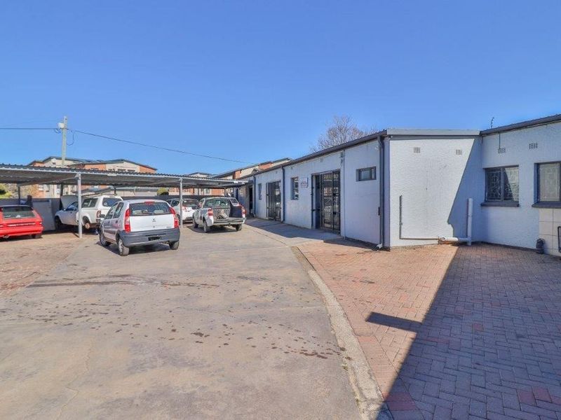 Rear exterior view of the business property featuring a paved driveway, covered carport parking area, and secure building access points.
