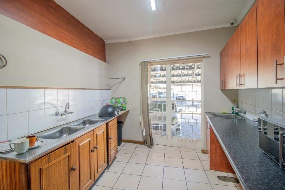 Functional kitchen featuring double stainless steel sinks, laminate countertops, ample wooden cabinetry, and direct access to the exterior through a security gate.