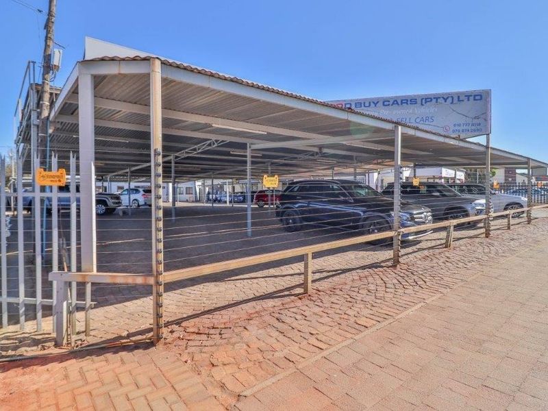 Commercial vehicle display area featuring a large steel carport structure, paved surface, and secure perimeter fencing with integrated electric security wires.