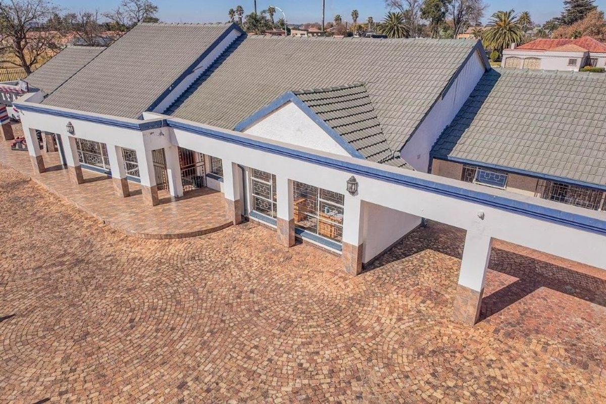 Aerial view of a commercial property featuring a tiled roof, extensive cobblestone driveway, and a covered entrance walkway with security gates.