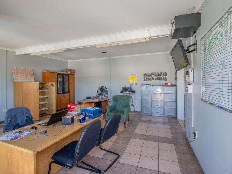 Functional office space featuring tiled flooring, wall-mounted television bracket, and basic utility lighting, suitable for a professional business environment.