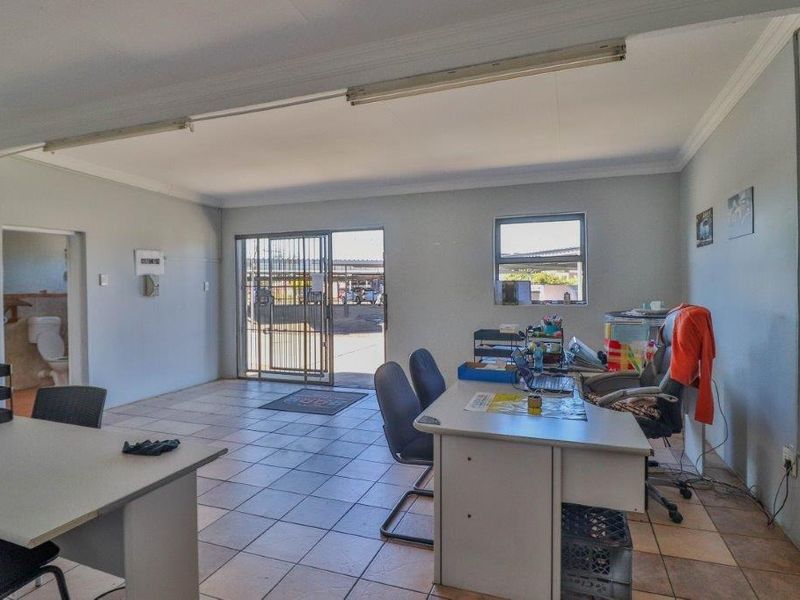 Functional office space featuring tiled flooring, security gate access, and integrated lighting, with an adjacent small restroom facility.