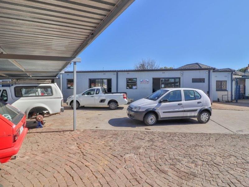 Rear exterior view of the business premises featuring a paved yard area and a covered carport structure.