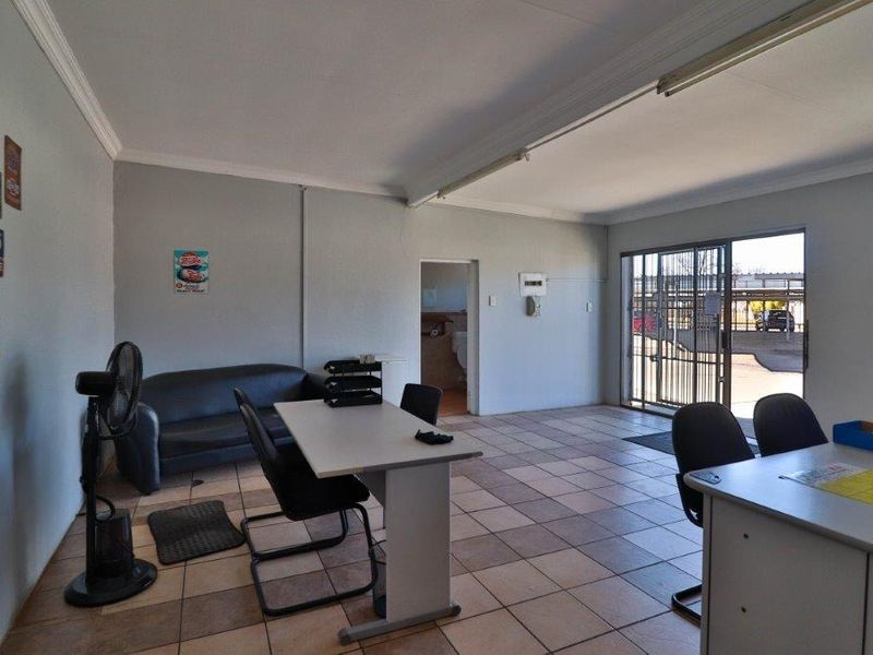 A functional office space featuring tiled flooring, a sliding glass door with security gate, and direct access to an adjacent room.