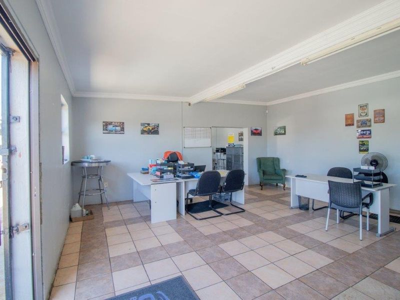 A functional office space featuring tiled flooring, fluorescent lighting, and a sliding glass door providing natural light and access.