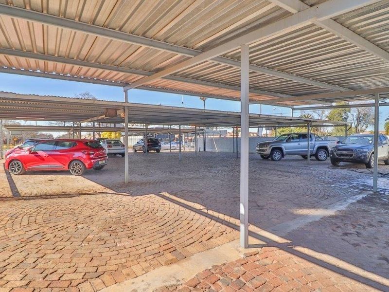 Covered outdoor parking area featuring a corrugated metal roof structure supported by steel columns with durable brick paved flooring.