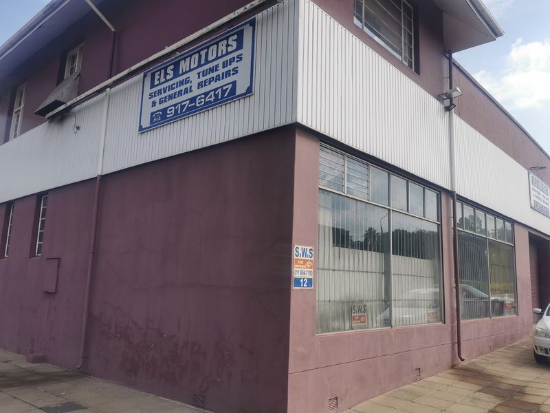 Industrial street-facing commercial property featuring large display windows, metal cladding, and prominent signage, showing signs of exterior wear and plaster cracking.