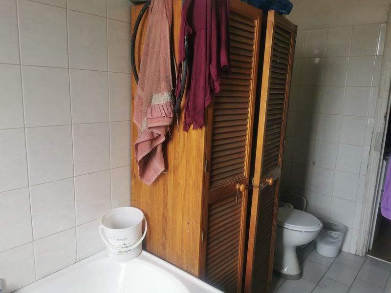 A dated bathroom featuring ceramic wall and floor tiles, a built-in wooden storage cabinet, a standard toilet, and a bathtub.