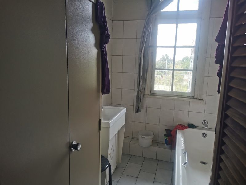 A dated bathroom featuring a bathtub, pedestal sink, and tiled finishes, requiring cosmetic updates to modernize the space.