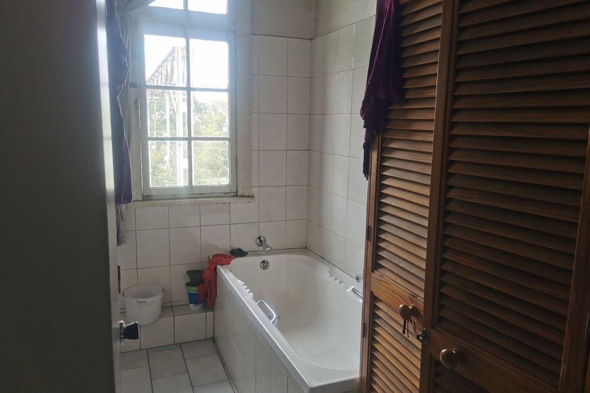 A dated bathroom featuring a built-in bathtub, tiled surfaces, and wooden louvered cabinetry, requiring cosmetic updates to modernize the space.