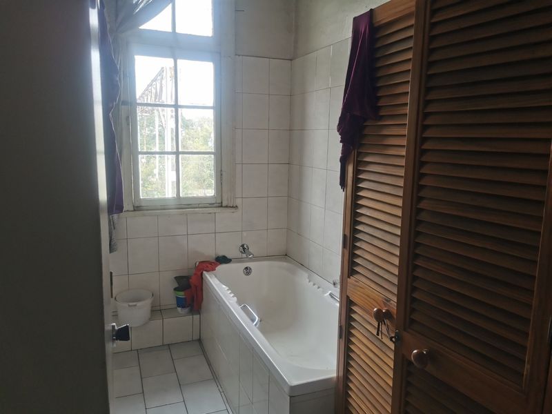 A dated bathroom featuring a built-in bathtub, tiled surfaces, and wooden louvered cabinetry, requiring cosmetic updates to modernize the space.