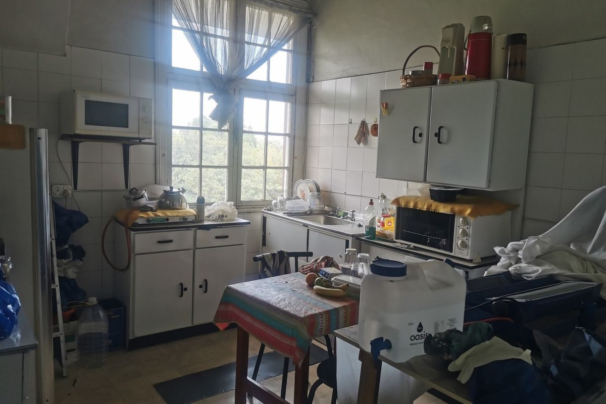 A dated kitchen featuring original cabinetry, tiled splashbacks, and a large window providing natural light, offering significant potential for modernization and renovation.
