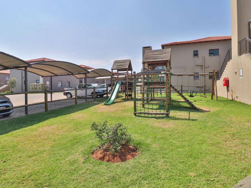 Communal outdoor area featuring a playground, lawn, and covered parking bays within the apartment complex.