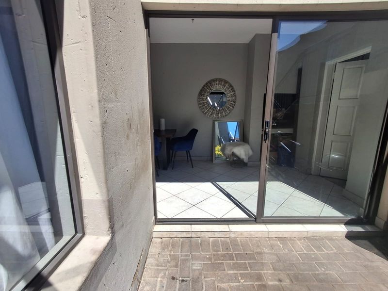 A view from a paved patio area looking through a sliding glass door into an interior living space with tiled flooring.