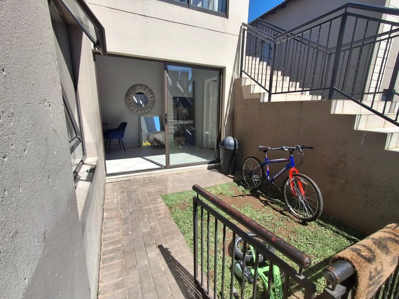 A compact ground-floor patio area featuring paved flooring, a sliding door entrance, and an adjacent small lawn space with metal staircase railings.