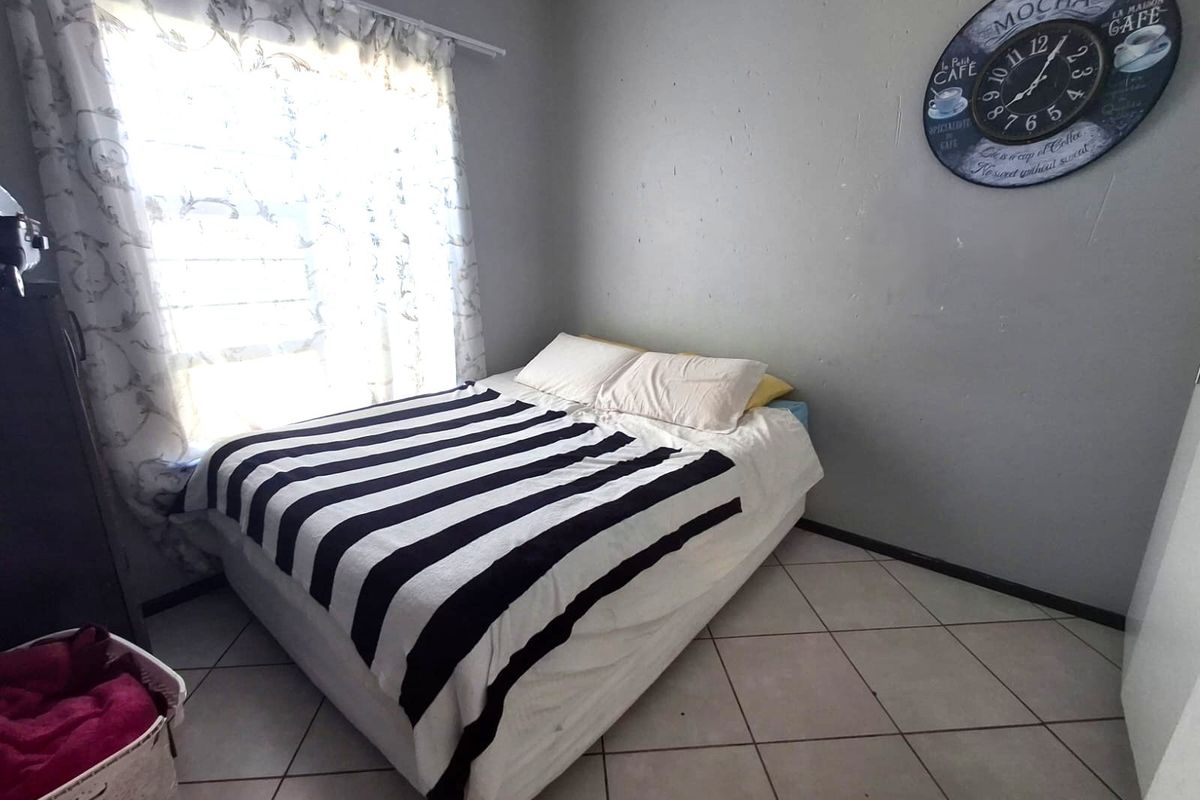 A functional bedroom featuring tiled flooring and a window with security bars, providing a simple and practical living space.