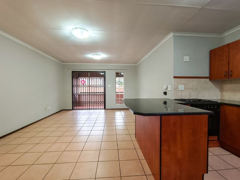 Spacious open-plan living area featuring tiled floors, a functional kitchen with granite countertops, and direct access to a balcony through a security gate.