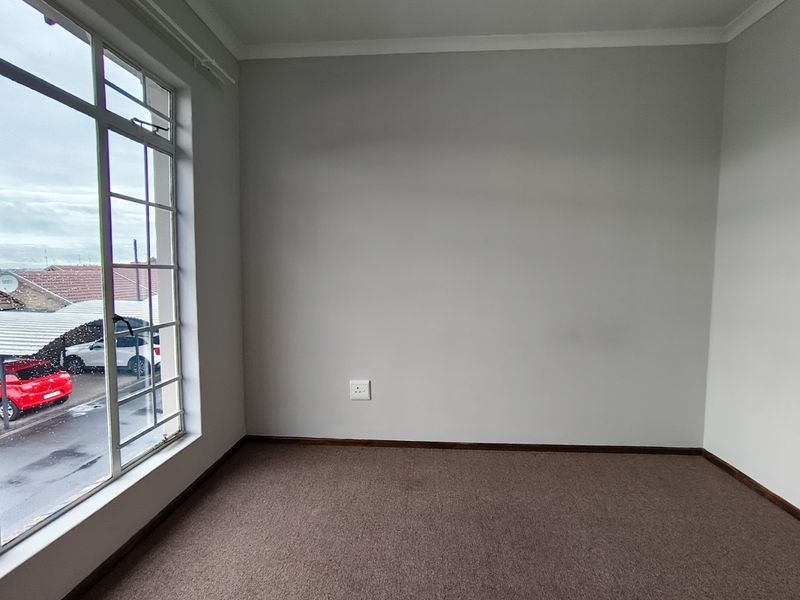 An empty bedroom featuring neutral walls, carpeted flooring, and a large multi-pane window providing natural light and a view of the exterior.