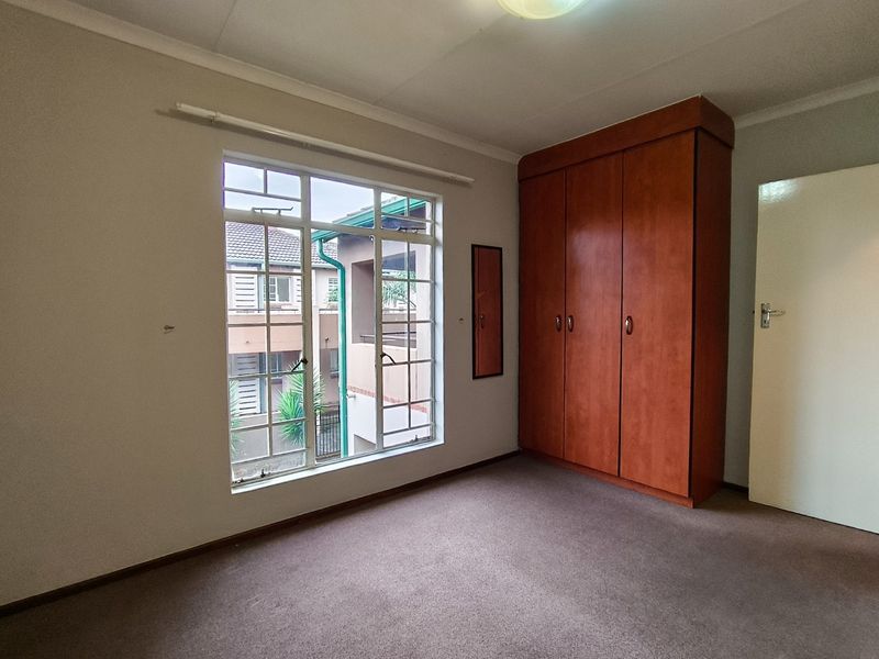 A vacant bedroom featuring a built-in wooden wardrobe, carpeted flooring, and a large multi-pane window providing natural light.