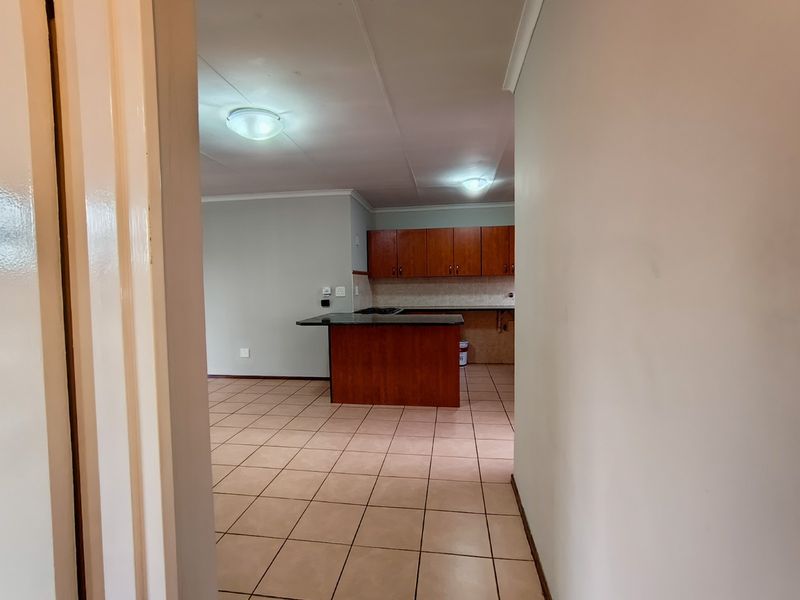 An open-plan living and kitchen area featuring tiled flooring, wooden cabinetry, and a breakfast bar, presented in a clean, vacant condition.