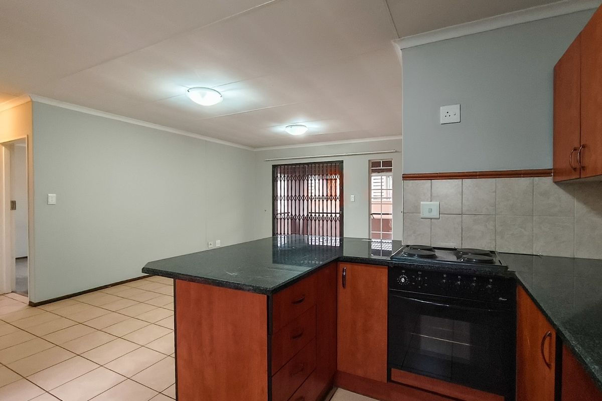 Open plan kitchen and living area featuring wooden cabinetry, granite countertops, built-in oven and stove, and tiled flooring throughout.