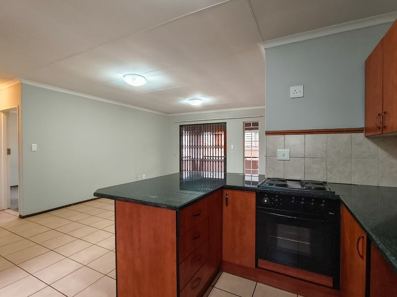 Open plan kitchen and living area featuring wooden cabinetry, granite countertops, built-in oven and stove, and tiled flooring throughout.