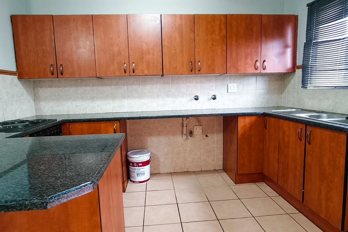 A functional kitchen featuring wood-finish cabinetry, granite countertops, tiled backsplash, and a double basin sink, offering a clean and practical workspace.
